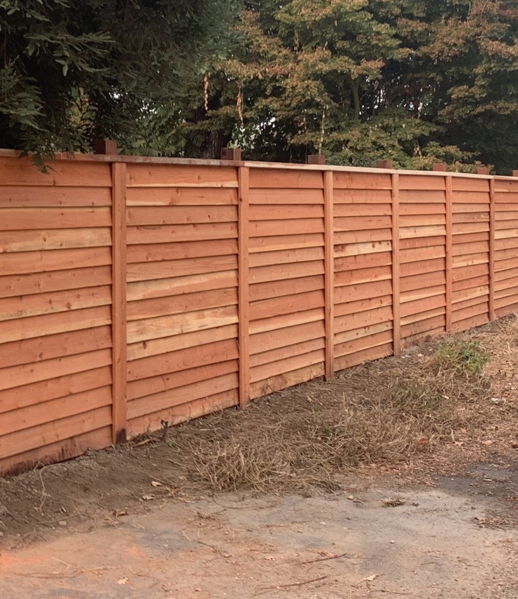 Newly installed horizontal redwood fence with square posts along an alley