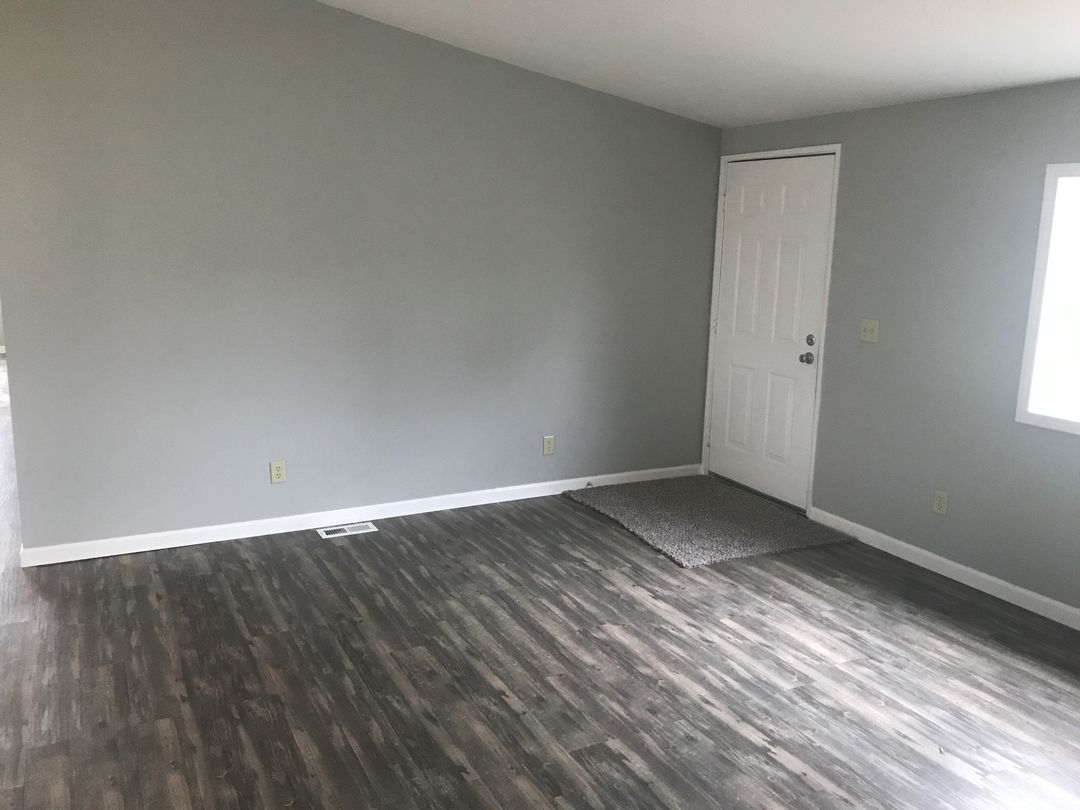 Living room freshly painted light gray with white baseboards and a white paneled door