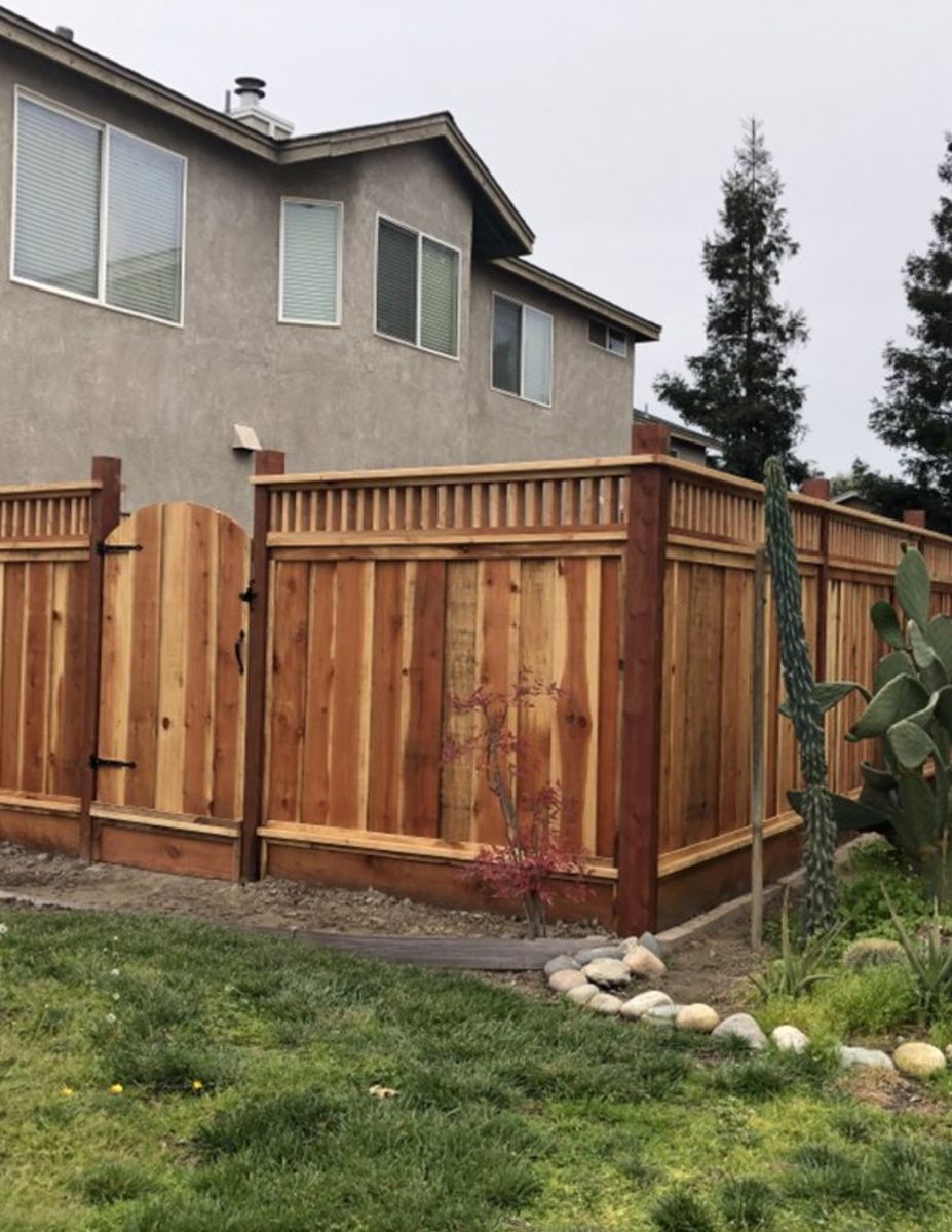 Redwood privacy fence with an arched gate and lattice top beside a two-story stucco home