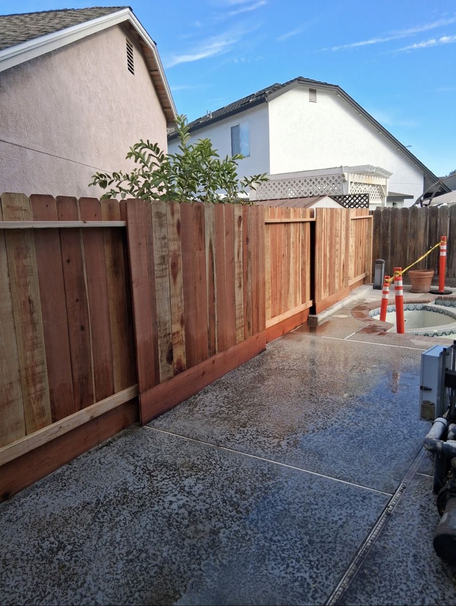 New redwood fence with a custom gate beside a backyard pool and spa area