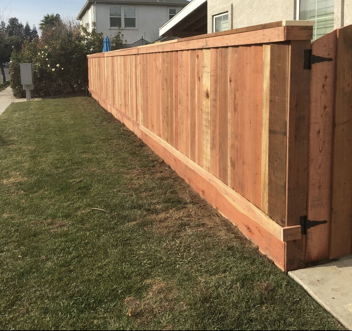 Long redwood privacy fence with a black-hinged gate running along the side of a stucco home