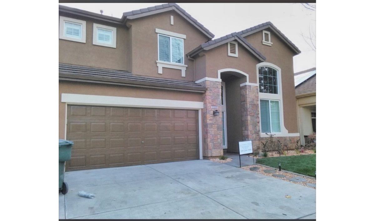 Two-story stucco home painted in warm brown and tan with stone accents