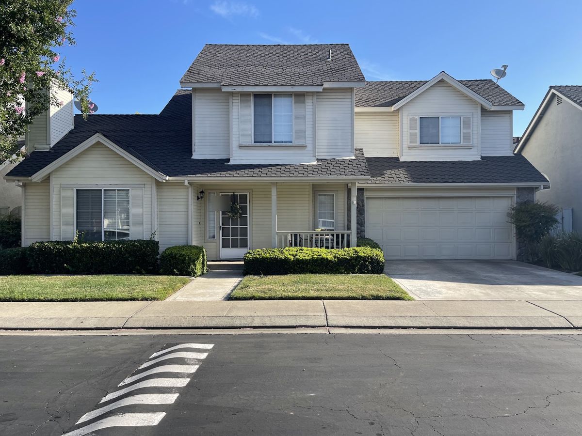 Two-story home with cream siding, dark roof and a covered front porch